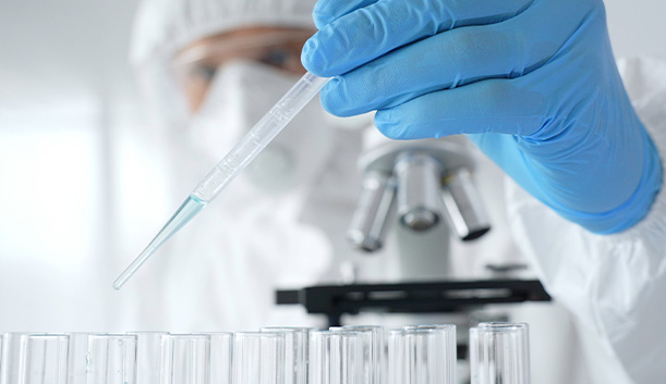 laboratory technician in protective gear using a pipette over test tubes for experiment analysis related to six samples